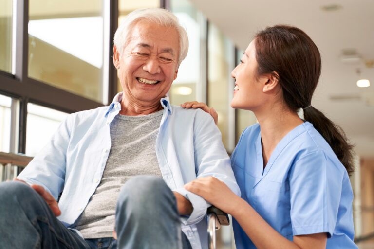 An Asian senior patient and caregiver smiling at each other