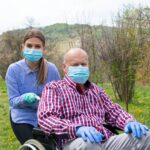 A caretaker and the senior go out in masks and gloves