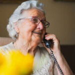 An old woman smiling and speaking on the telephone