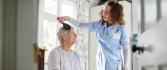 A nurse is combing the hair of an older woman.