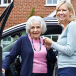 An old woman getting down the car with the help of the lady