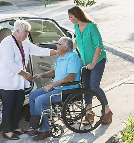 A man in a wheelchair being assisted by two women.