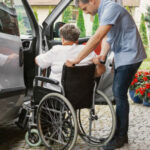 A man moving the lady in a wheelchair to the car