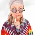 A woman with glasses and a tie dye shirt smoking.