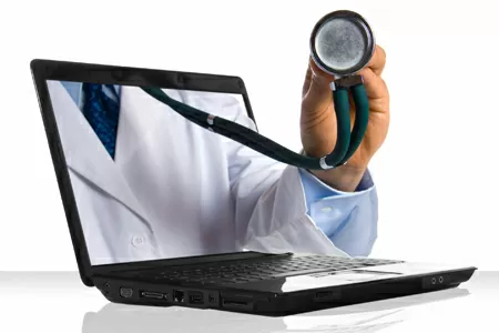 A person holding a stethoscope in front of a laptop.