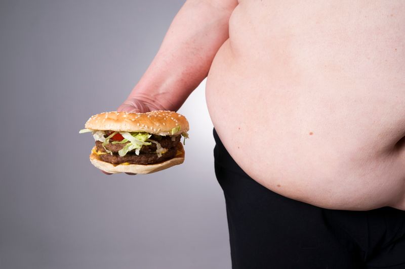 An obese belly and holding the cheeseburger in his hand