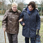 A woman holding an old woman's hand and walking