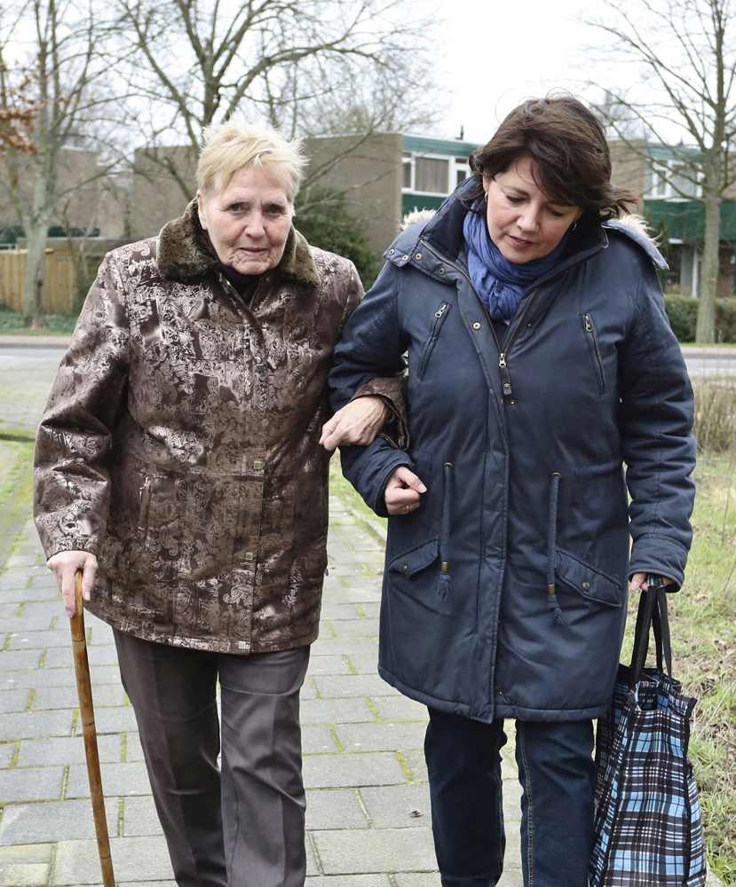 A woman holding an old woman's hand and walking