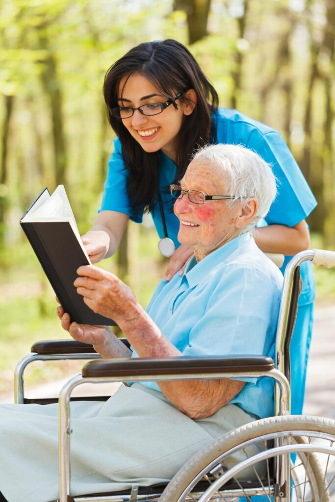 elderly woman in wheelchair reading a book with cargiver - Companion Care Service for Carmel CA