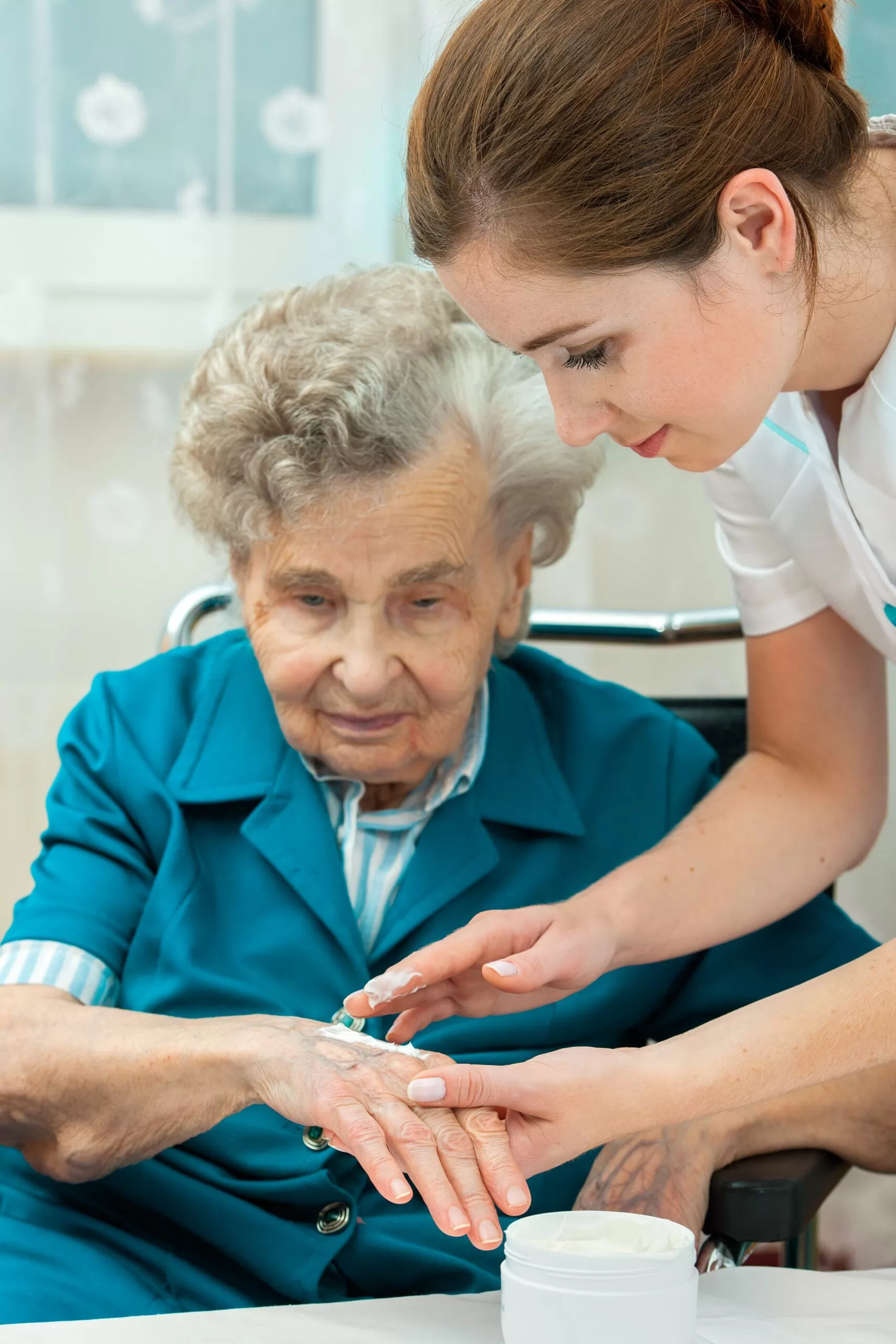 A nurse applying cream on the elderly woman hand